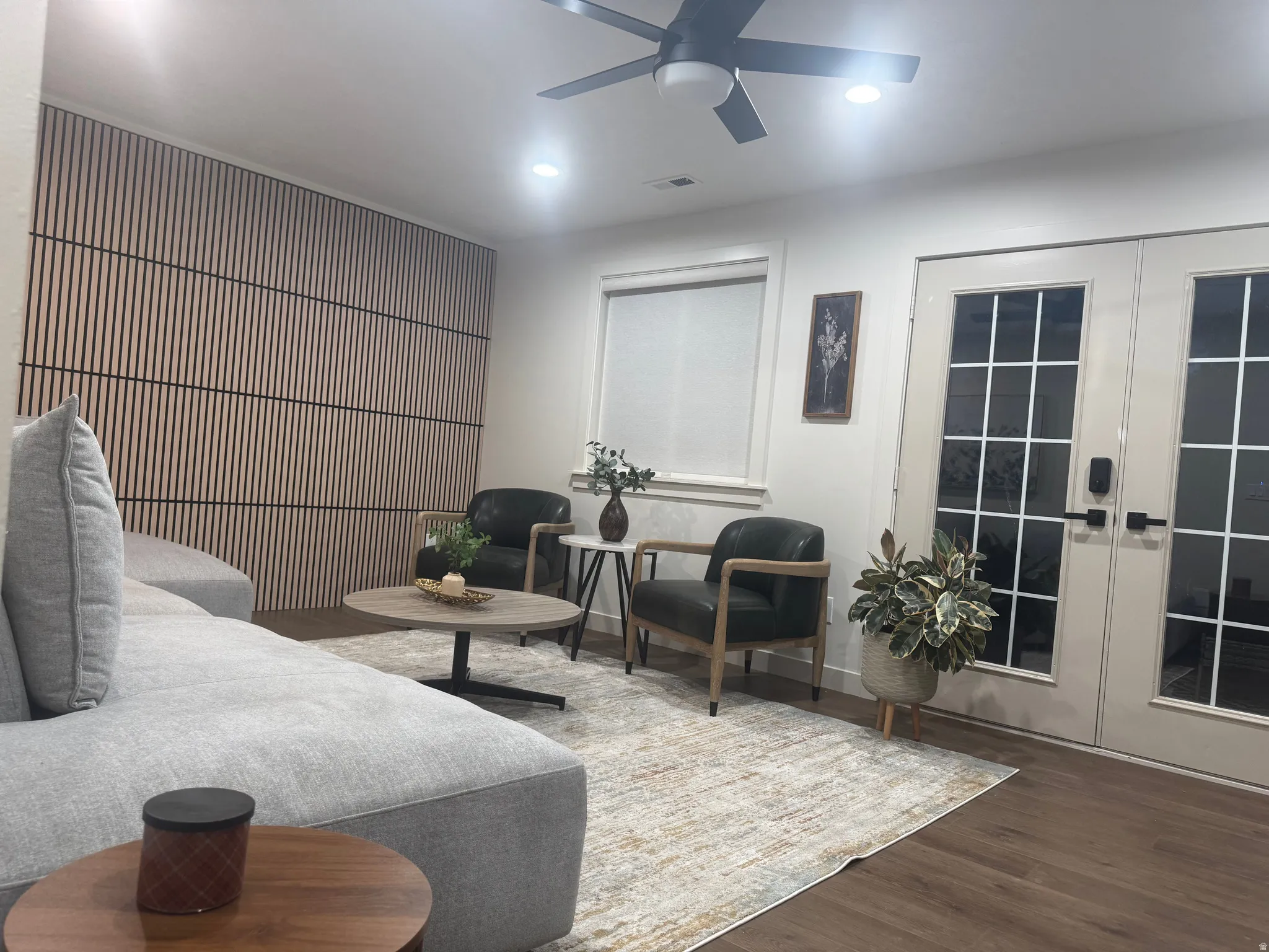 Living area featuring wood-finish flooring, a contemporary accent wall with vertical slat detailing, and a modern ceiling fan