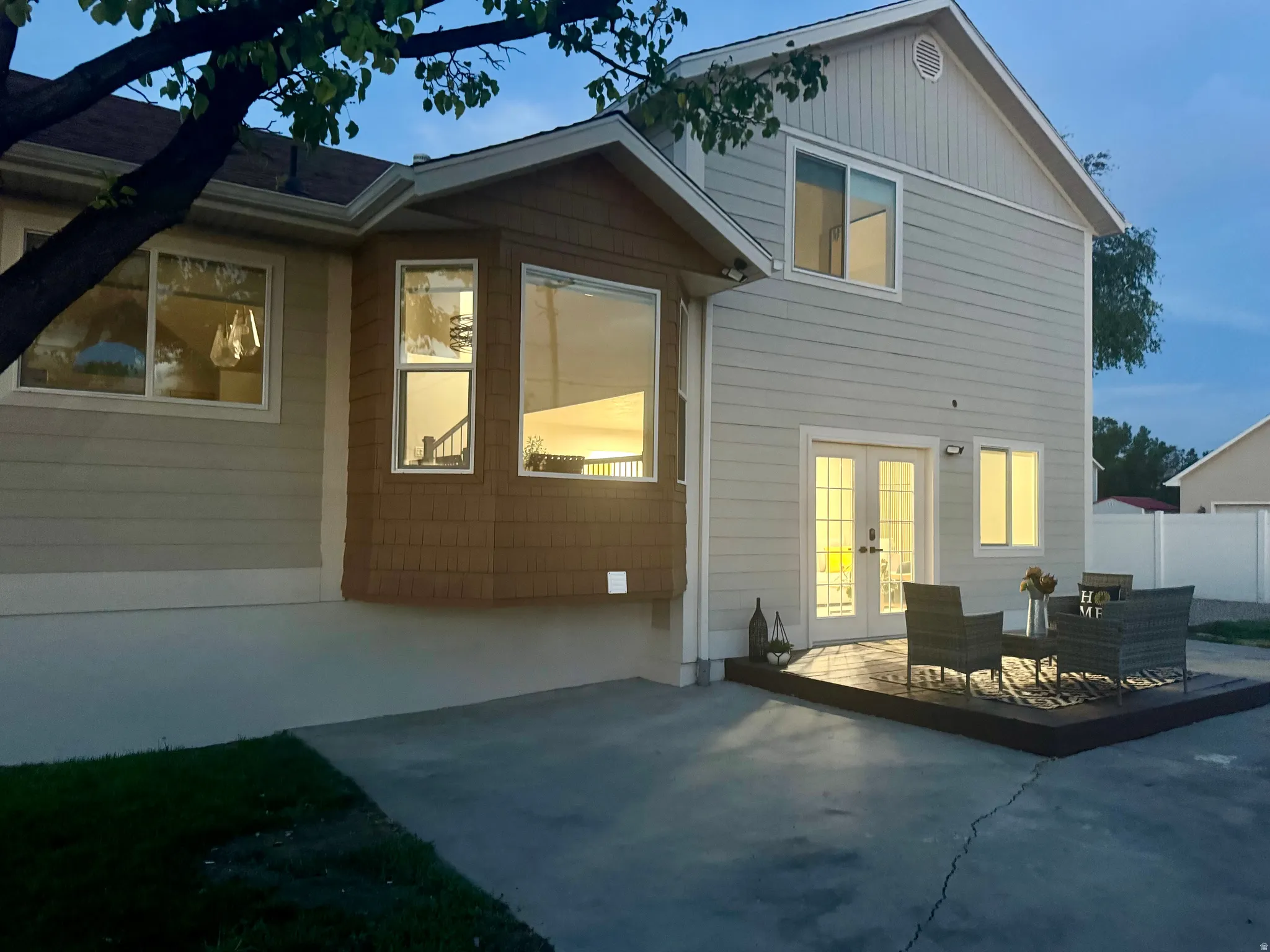 Rear exterior featuring a ground-level wood-finish deck, concrete patio, and white French doors