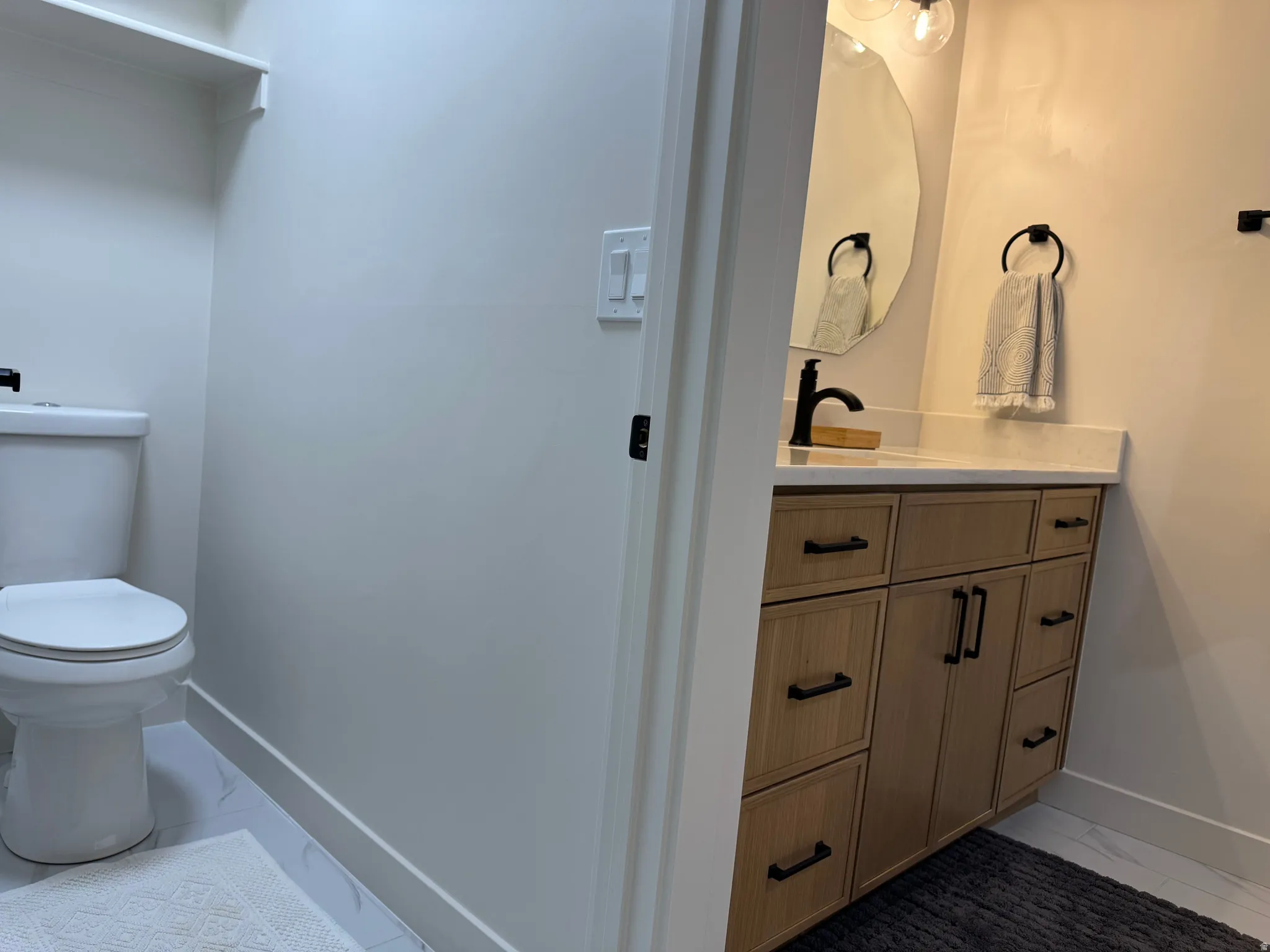 Modern vanity featuring wood-finish cabinetry with matte black hardware, a light-toned countertop, and an irregular shaped mirror