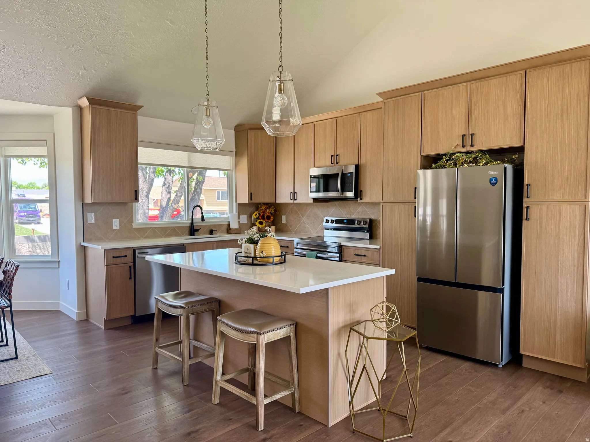 Kitchen featuring wood-finish flooring, light-toned cabinetry, stainless steel appliances, a center island with countertop seating, and a diamond-patterned backsplash