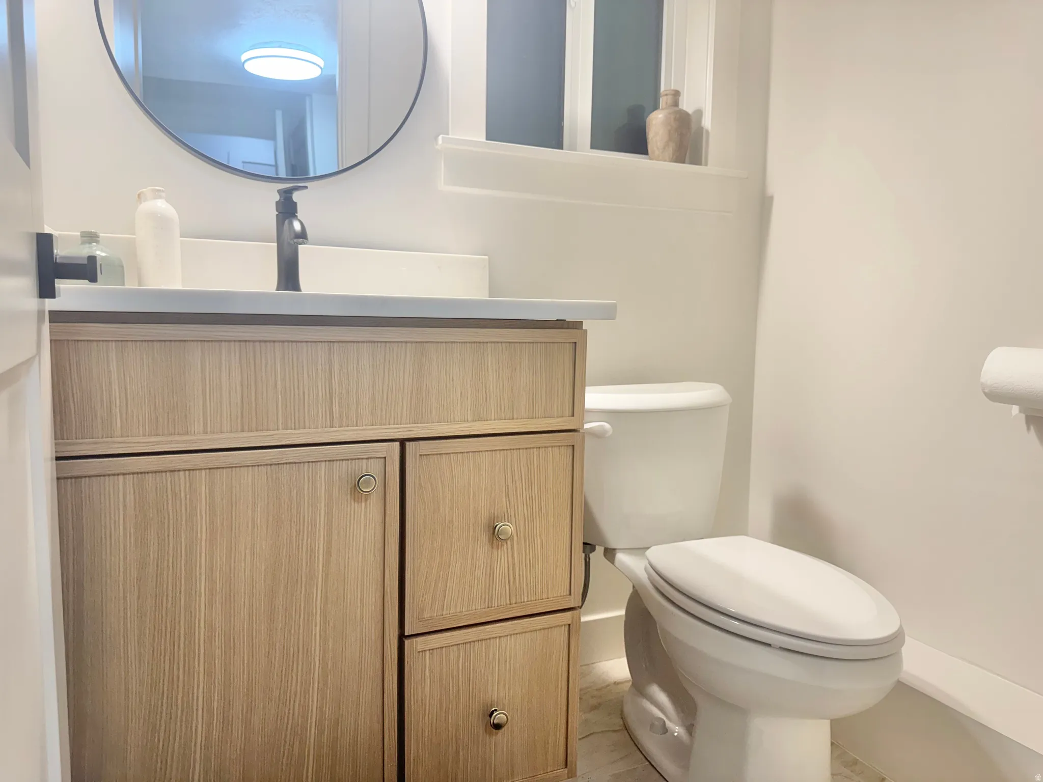 Modern bathroom featuring a wood-finish vanity with ample storage, a white countertop, and matte black fixtures