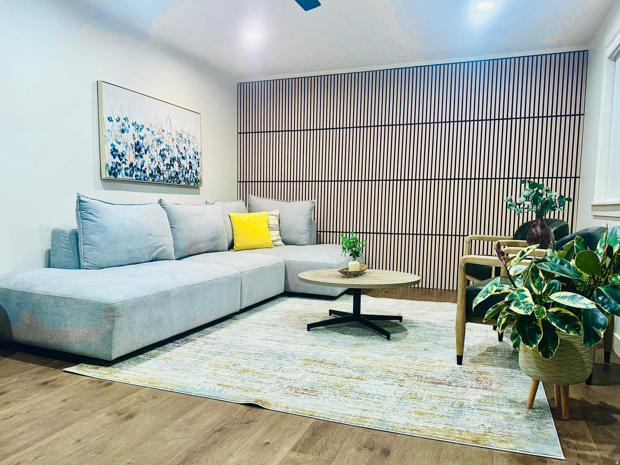 Interior living space featuring wood-finish flooring, a contemporary accent wall with vertical slat detailing, recessed lighting, and a window with white trim
