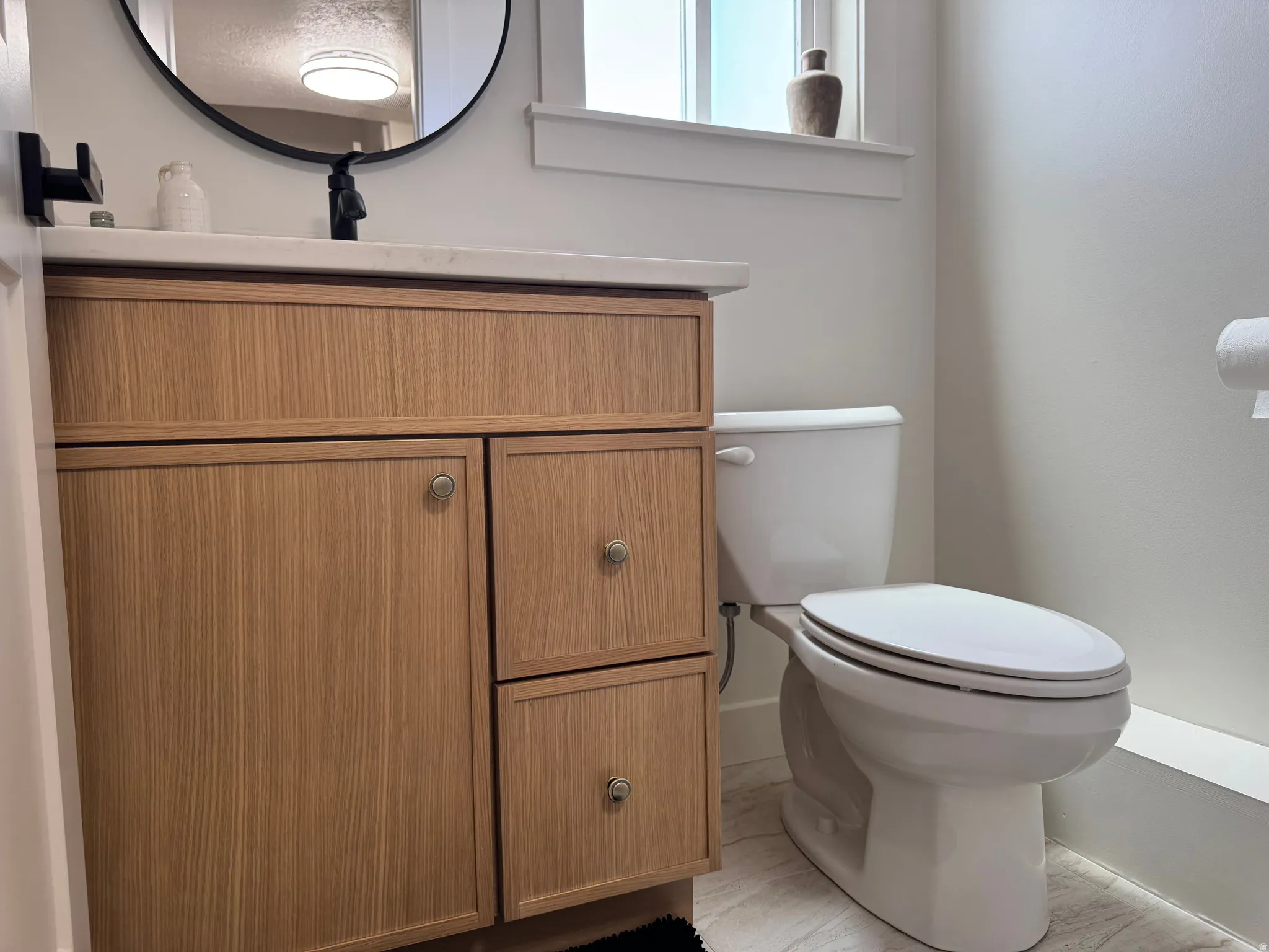 Bathroom featuring a wood-finish vanity with a light countertop, a contemporary round mirror, and a modern black faucet