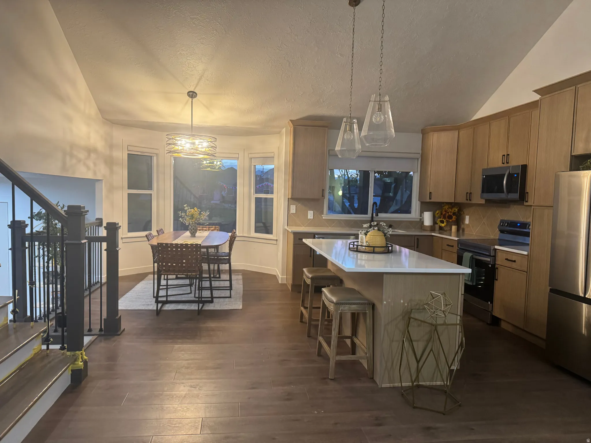 Kitchen featuring light wood-finish cabinetry, stainless steel appliances, a white island with seating, a diagonal tile backsplash, and wood-finish flooring
