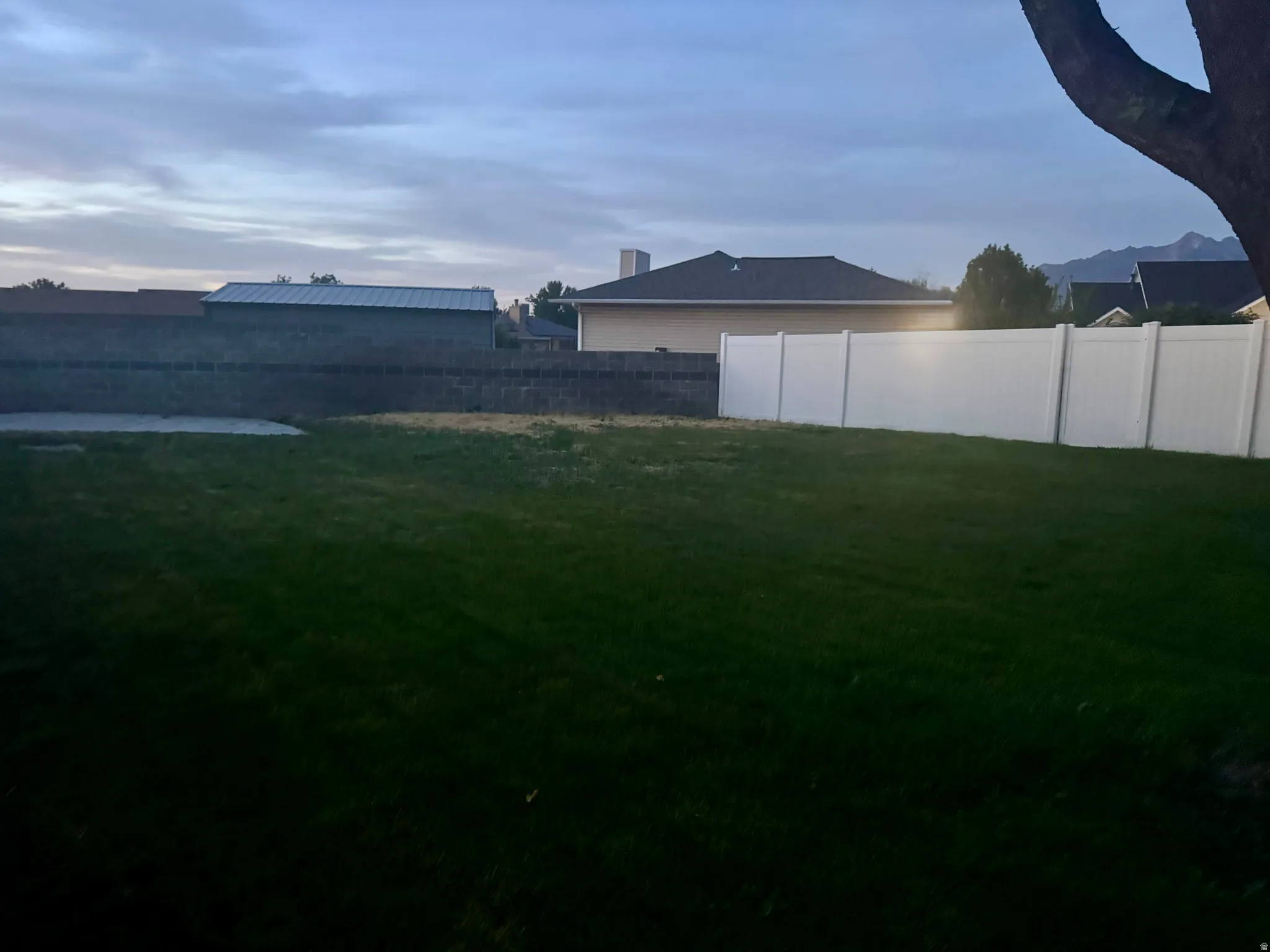 Expansive yard featuring a large grassy area, a concrete pad, and a white privacy fence