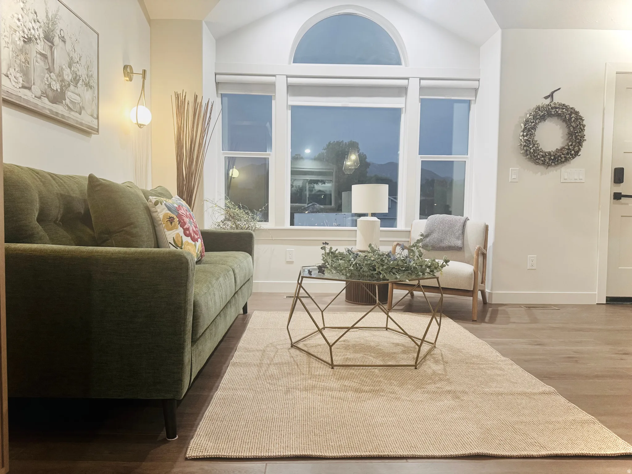 Spacious living area featuring expansive windows with an arched transom, wood-finish flooring, and white baseboards