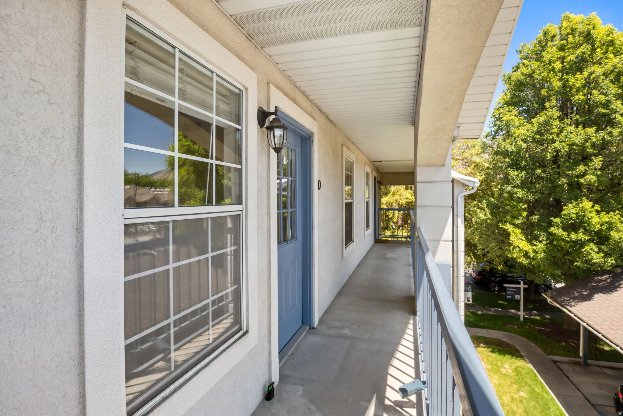 Exterior walkway featuring stucco siding, multiple windows with white grilles, and a blue entryway door with glass paneling