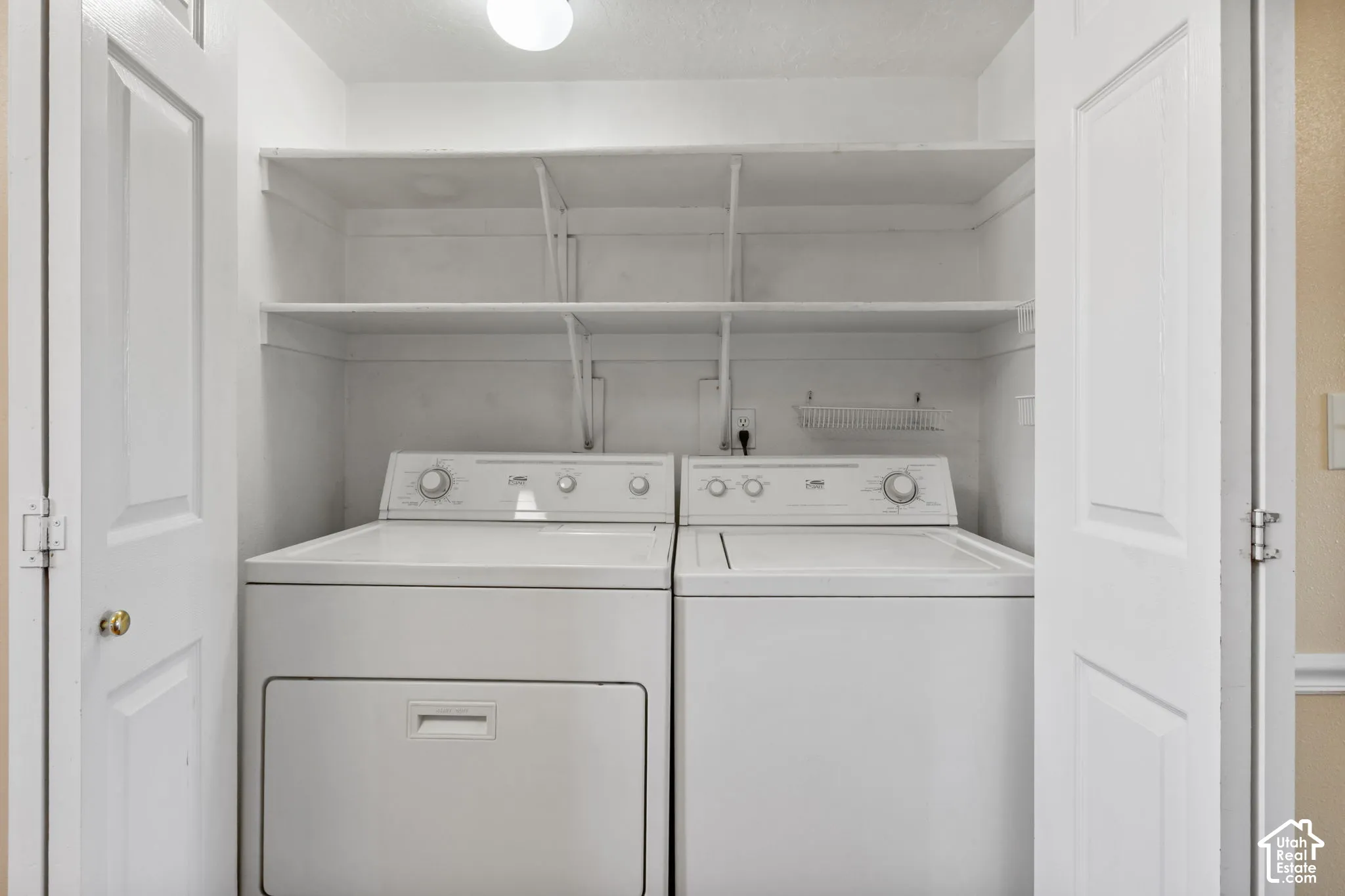 Laundry closet featuring a built-in washer and dryer set, two adjustable storage shelves, and overhead lighting