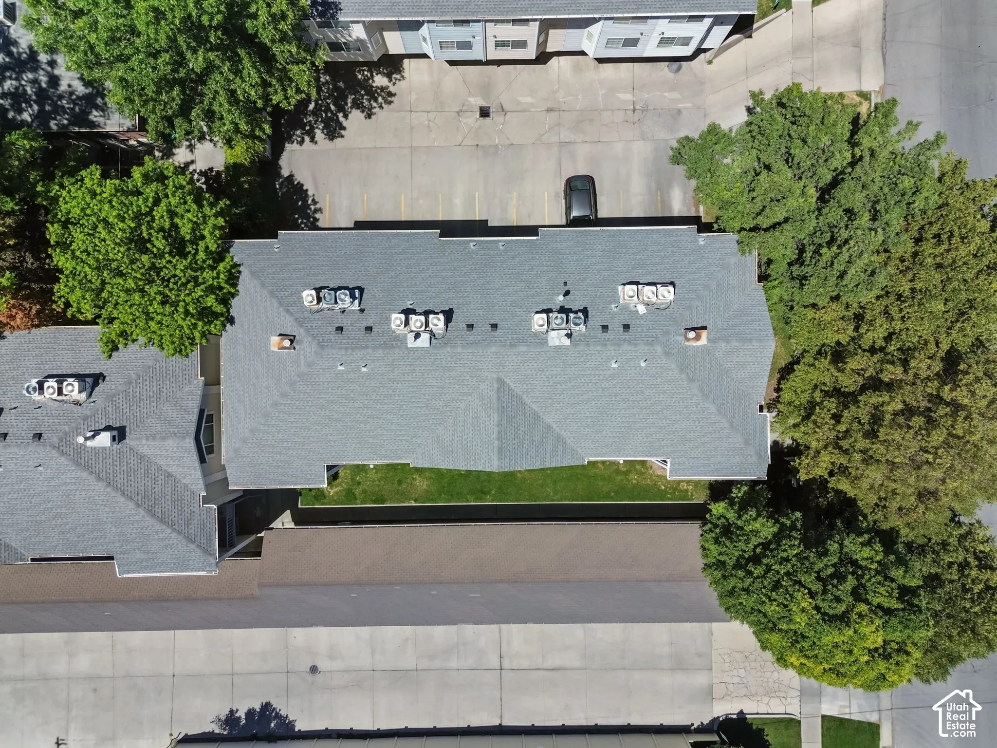 Building with a gray shingle roof, multiple rooftop HVAC units, and surrounding paved parking areas