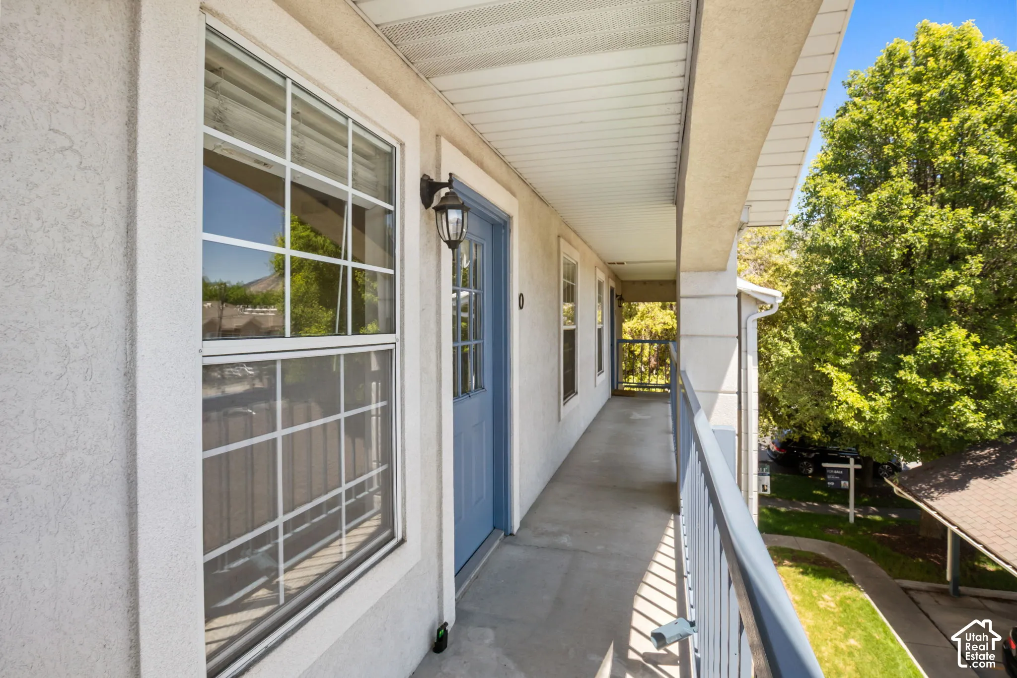 Exterior walkway featuring stucco siding, multiple windows with white grilles, and a blue entryway door with glass paneling