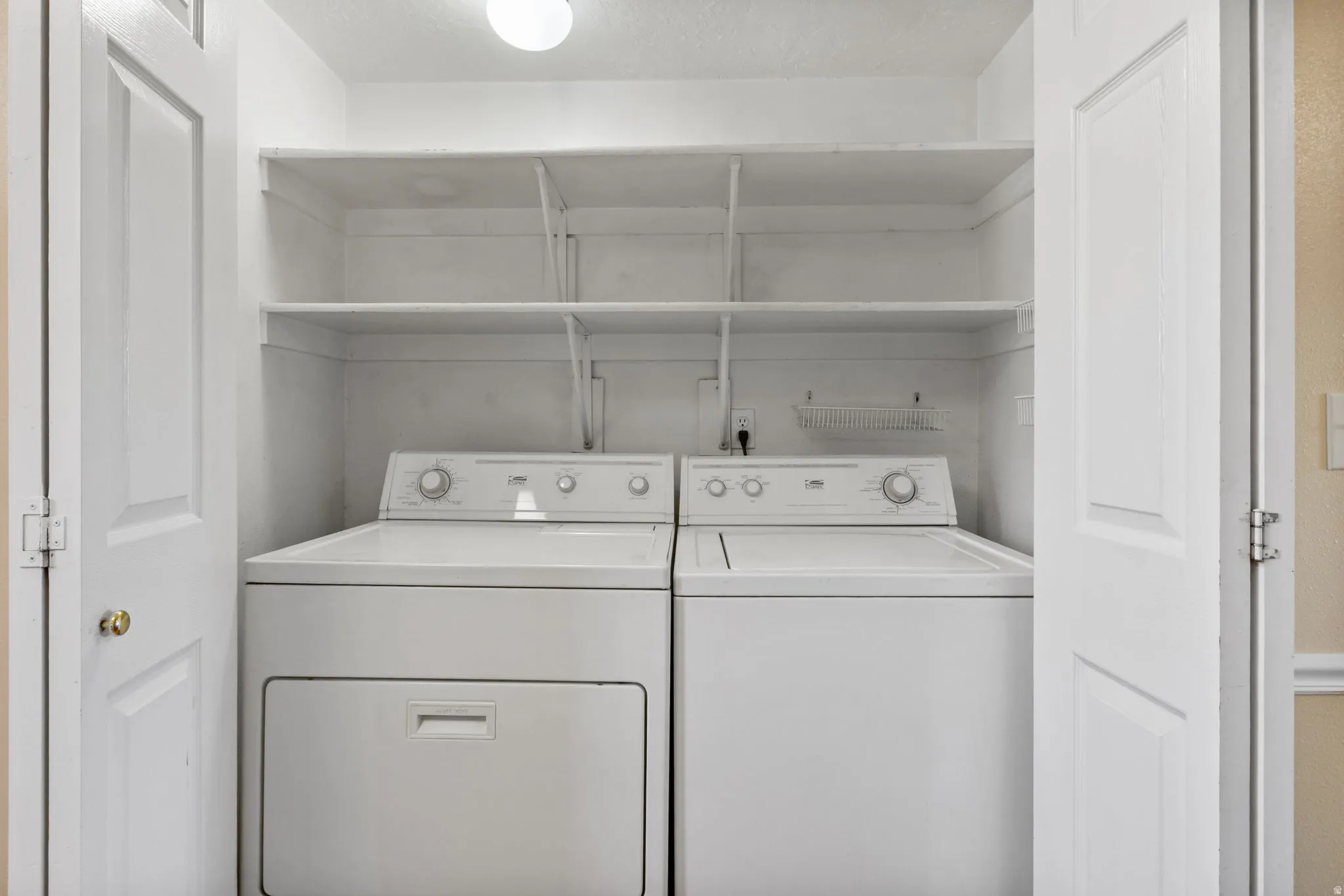 Laundry closet featuring a built-in washer and dryer set, two adjustable storage shelves, and overhead lighting