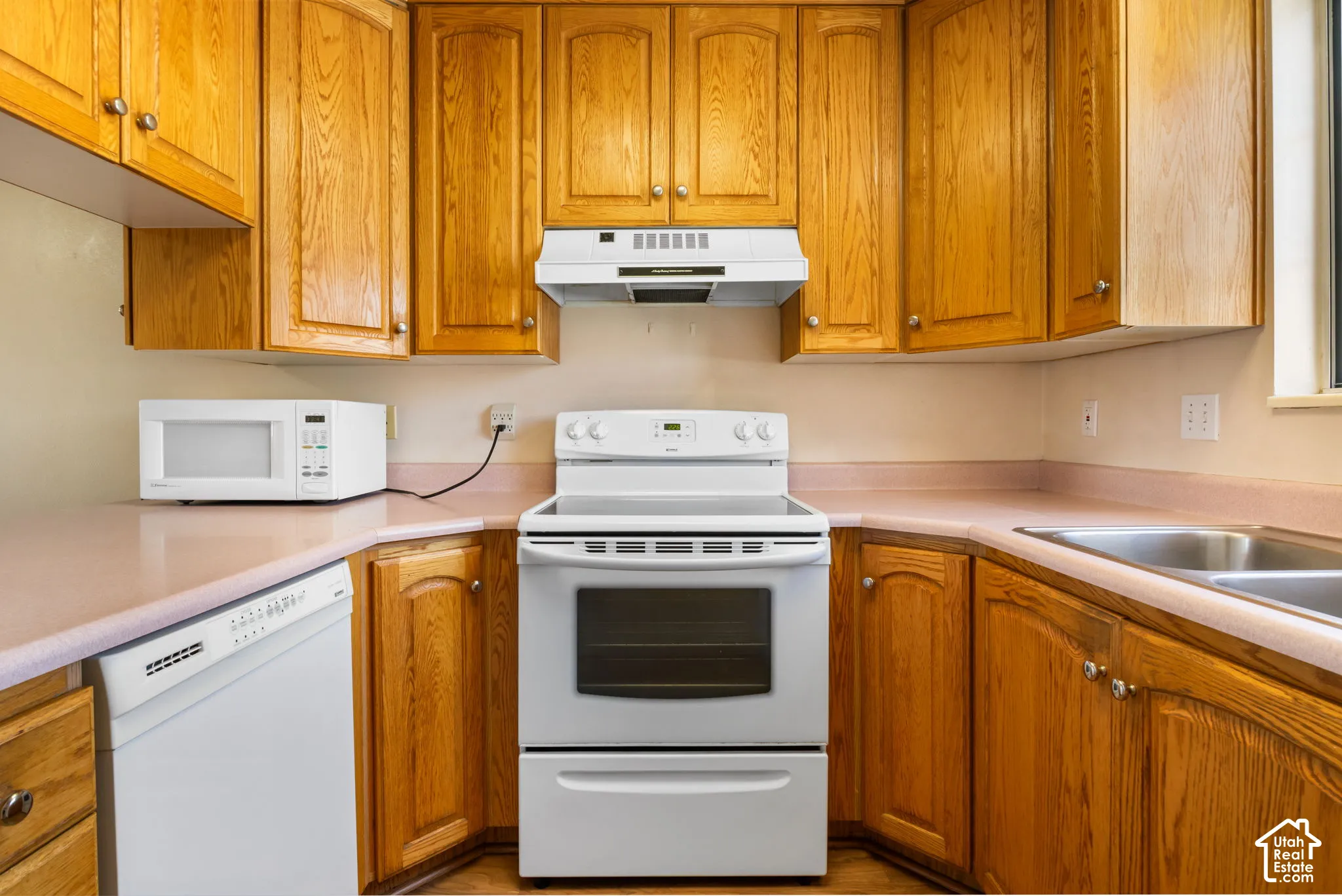 Kitchen featuring warm wood cabinetry, light-toned countertops, a white electric range, and a double basin stainless steel sink