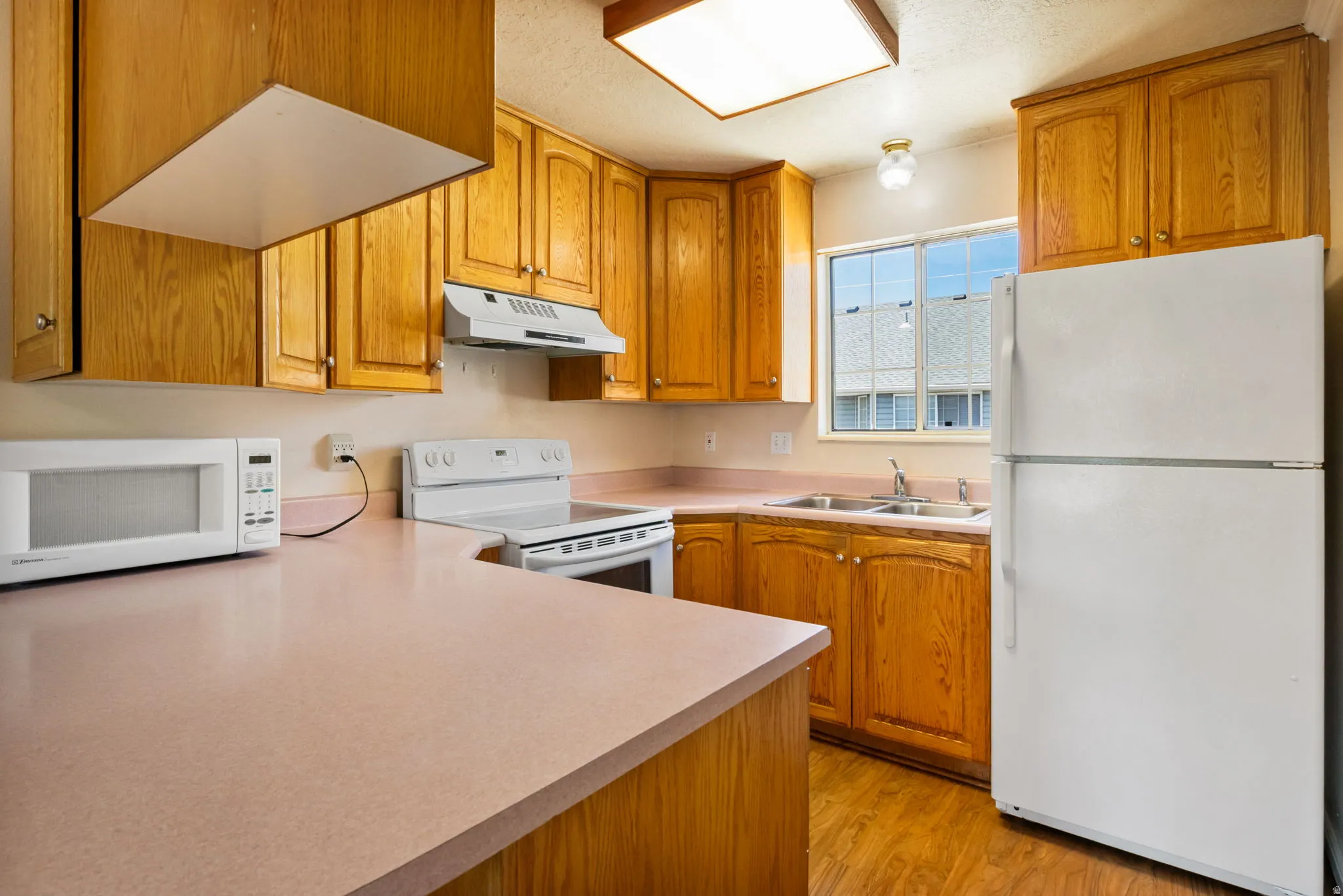 Kitchen featuring wood-finish cabinetry, a double basin sink, light-toned countertops, a white range with an overhead vent, and wood-finish flooring