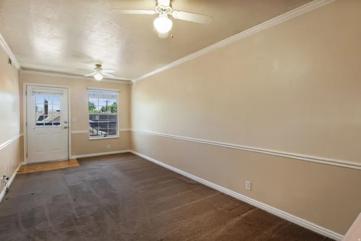 Spacious room featuring neutral paint, crown molding, chair rail molding, two ceiling fans, and a glass-paneled exterior door