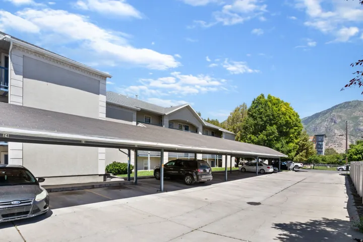 Covered parking structure with individual numbered spaces, concrete pavement, and an adjacent multi-story building featuring light-colored exterior siding