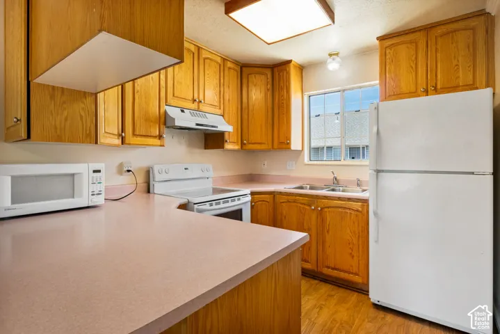 Kitchen featuring wood-finish cabinetry, a double basin sink, light-toned countertops, a white range with an overhead vent, and wood-finish flooring