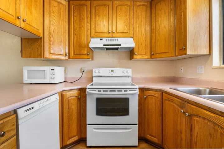Kitchen featuring warm wood cabinetry, light-toned countertops, a white electric range, and a double basin stainless steel sink