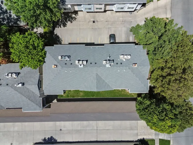 Building with a gray shingle roof, multiple rooftop HVAC units, and surrounding paved parking areas