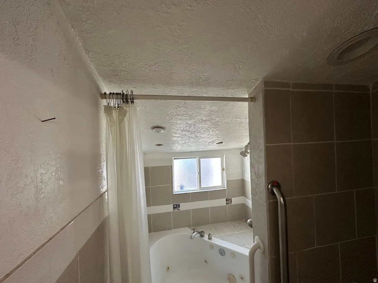 Bathroom featuring a corner jetted tub, tiled surround, and frosted window