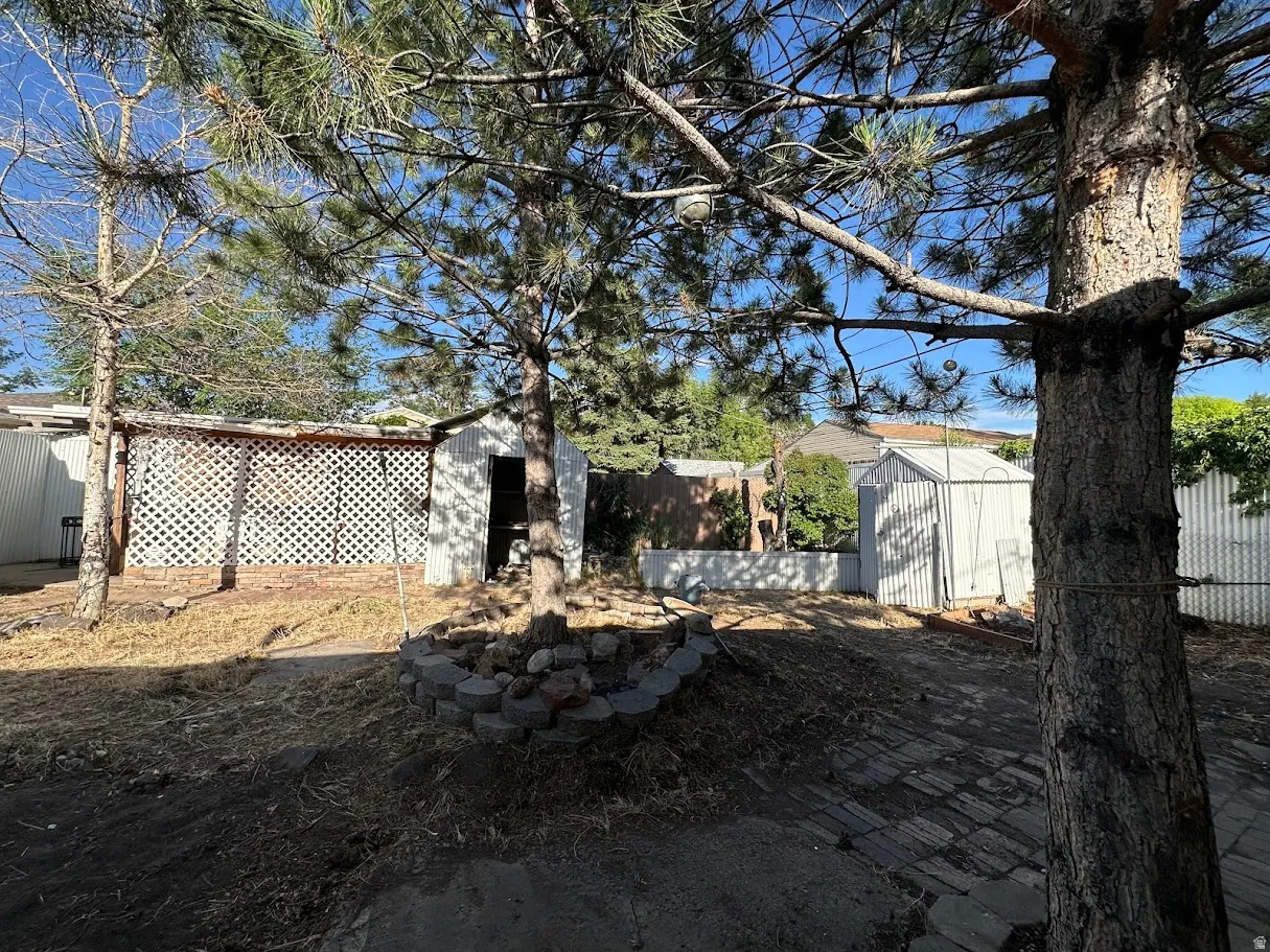 Spacious yard featuring mature trees, a latticework structure, two storage sheds, and a paver patio area