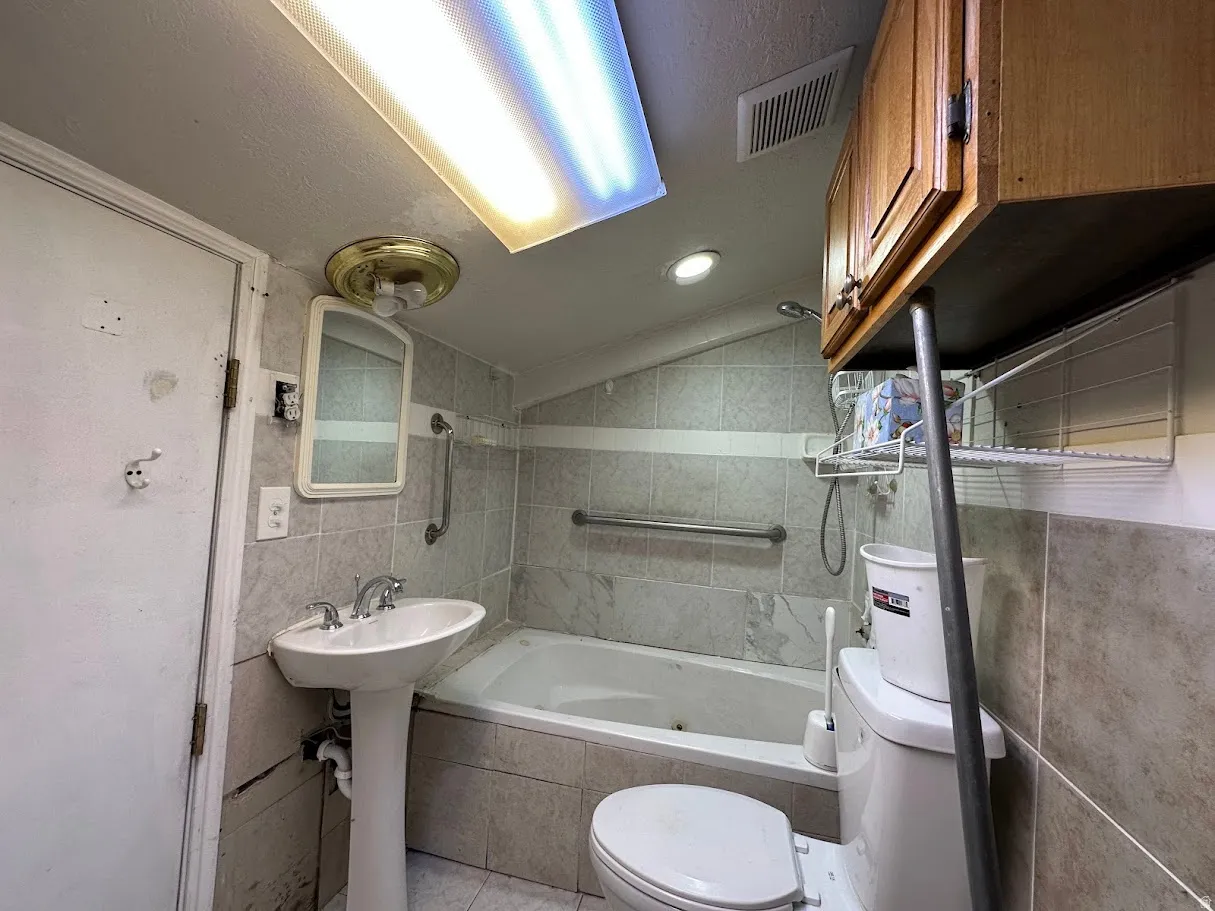 Bathroom featuring a pedestal sink, white bathtub, wall-mounted mirror, and tiled walls