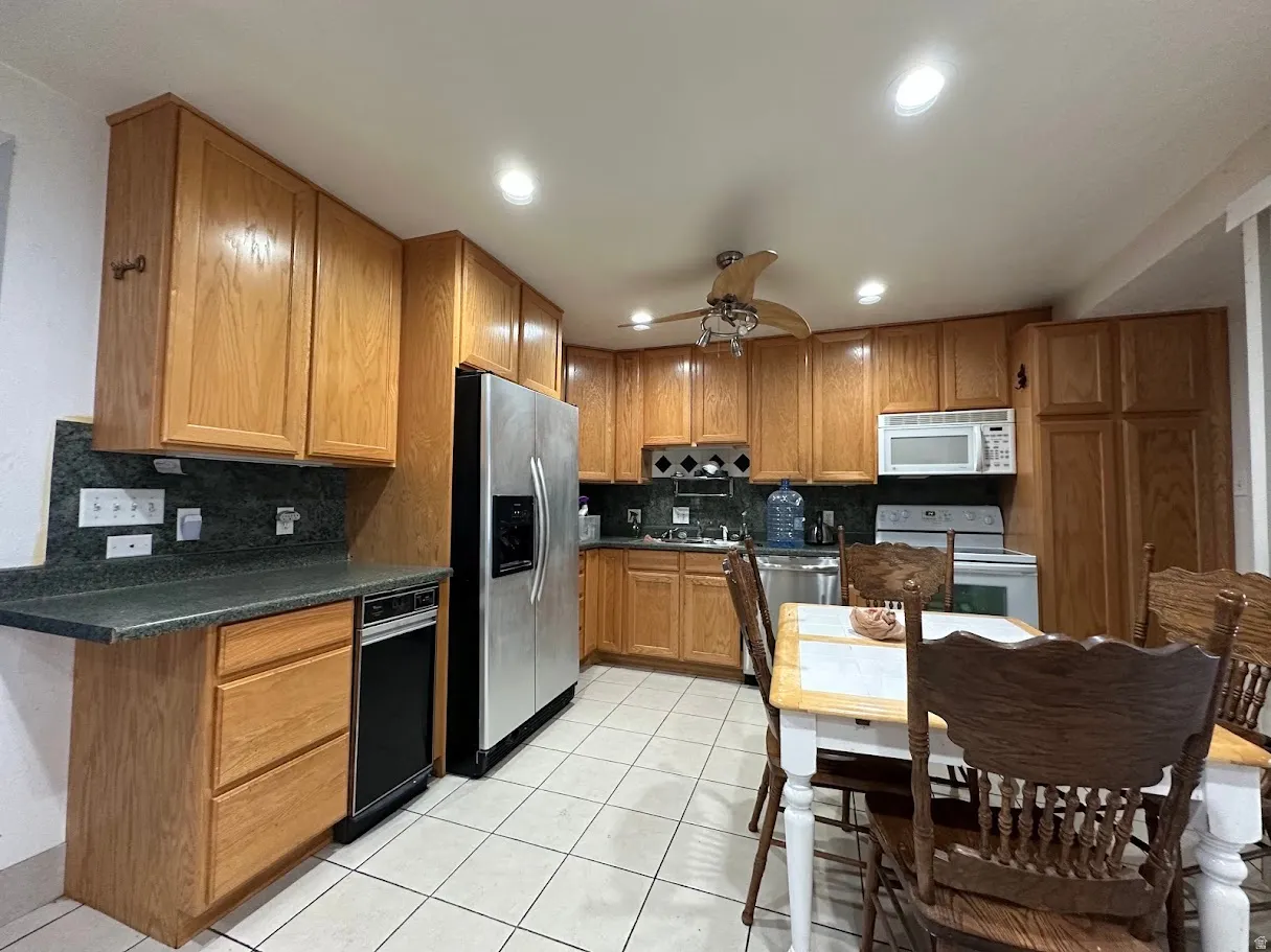 Kitchen featuring wood cabinetry, stainless steel refrigerator, white tile flooring, recessed lighting, and a ceiling fan