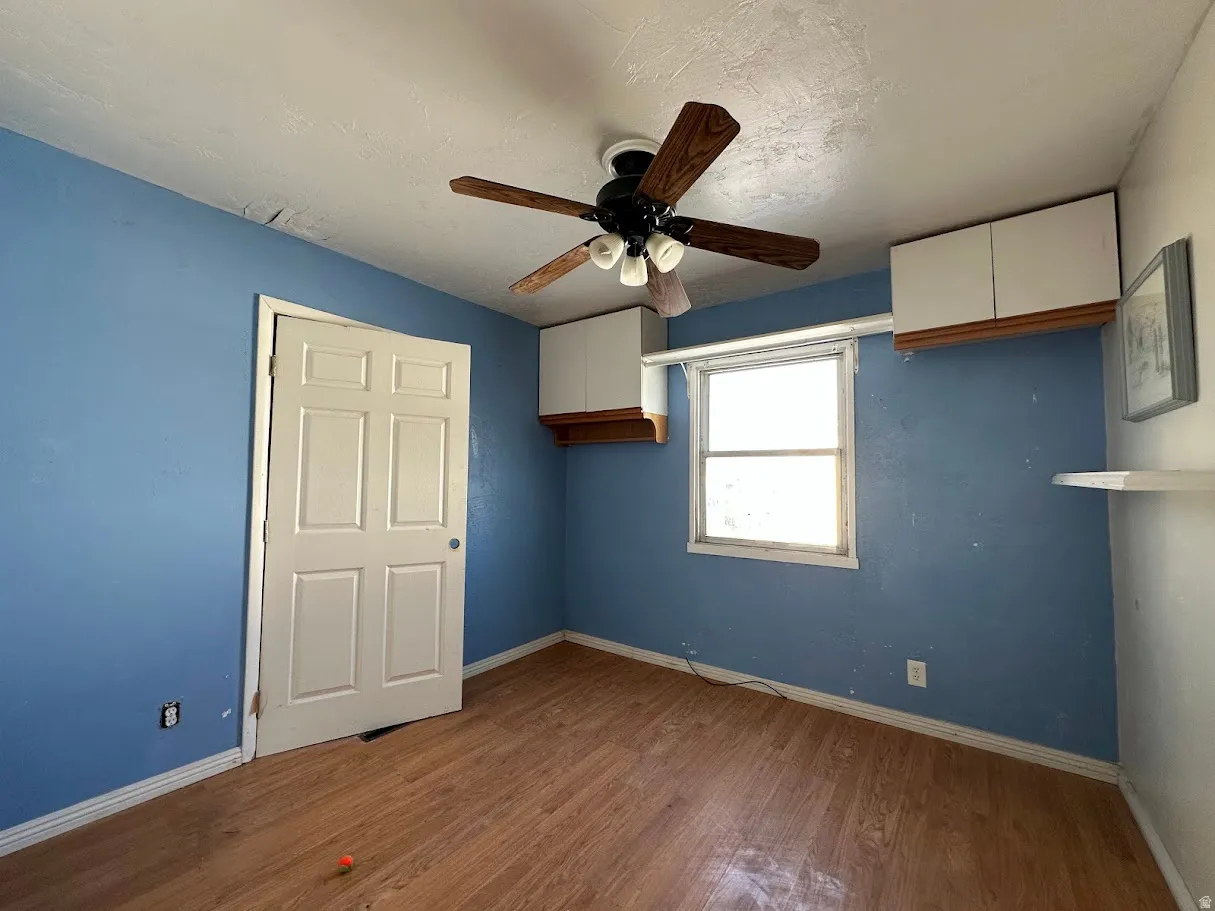 Interior room featuring wood-finish flooring, a ceiling fan with light kit, a window, and white built-in wall cabinetry