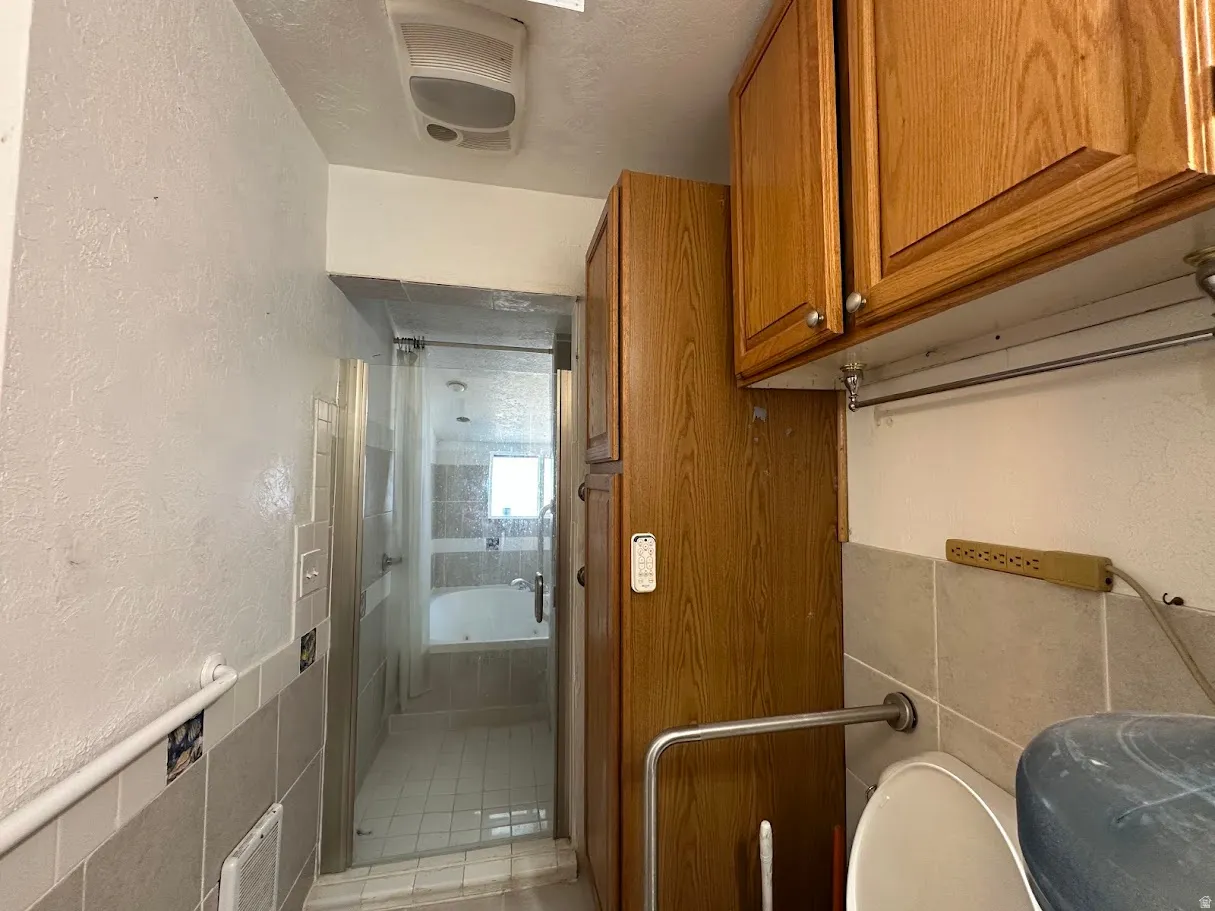 Bathroom featuring a glass-enclosed shower, built-in soaking tub, wood-finish cabinetry, and tiled walls