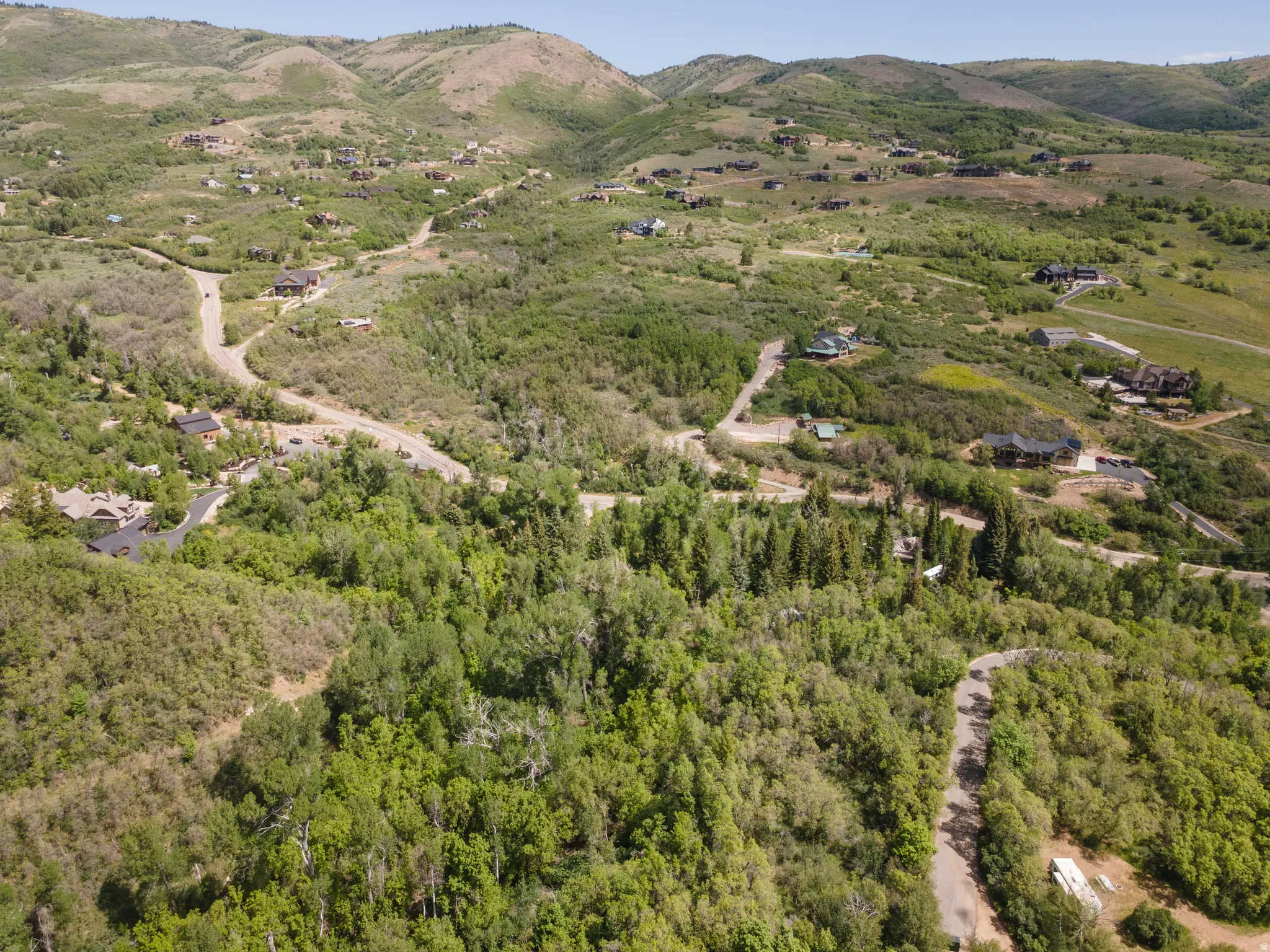 Expansive mountainous terrain featuring scattered residential properties, winding roads, and dense tree coverage