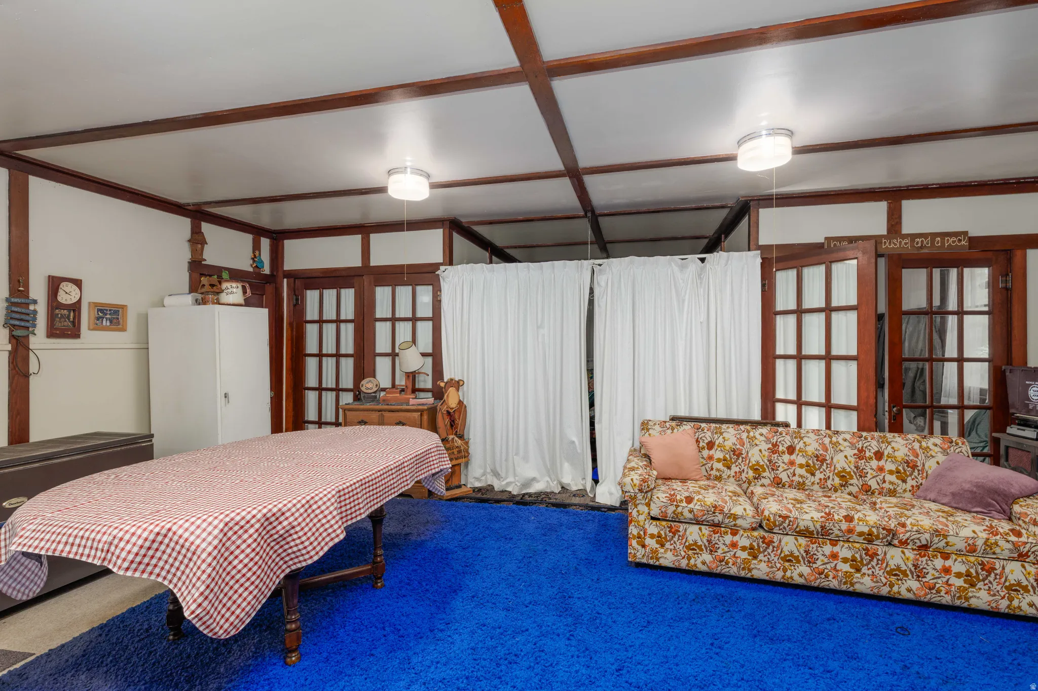 Exposed beam ceiling with white panels, multiple light fixtures, contrasting wood trim throughout, and two sets of double French doors with grid-patterned glass