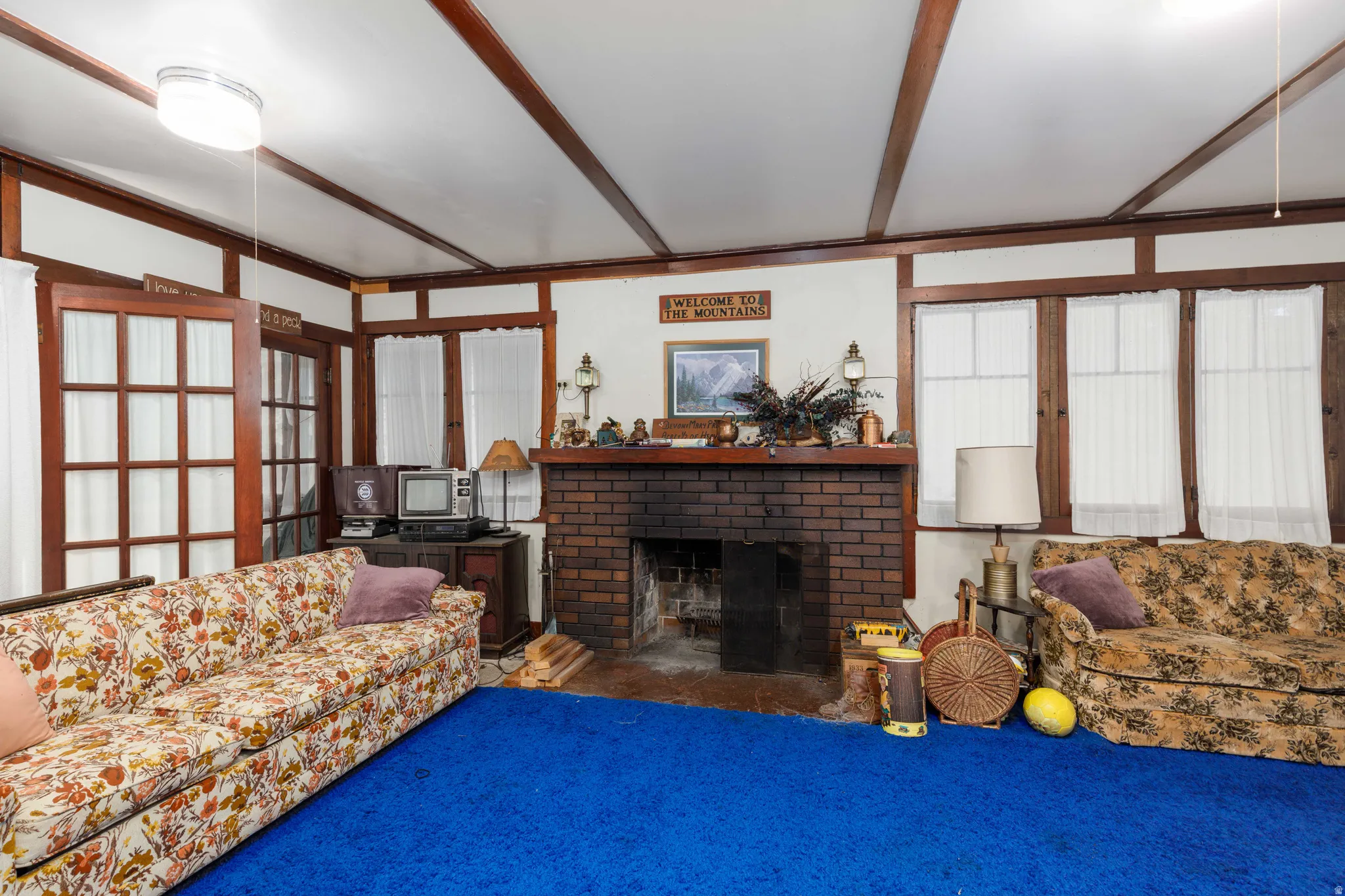 Living area featuring a floor-to-ceiling brick fireplace, wood-beamed ceiling, and multiple windows