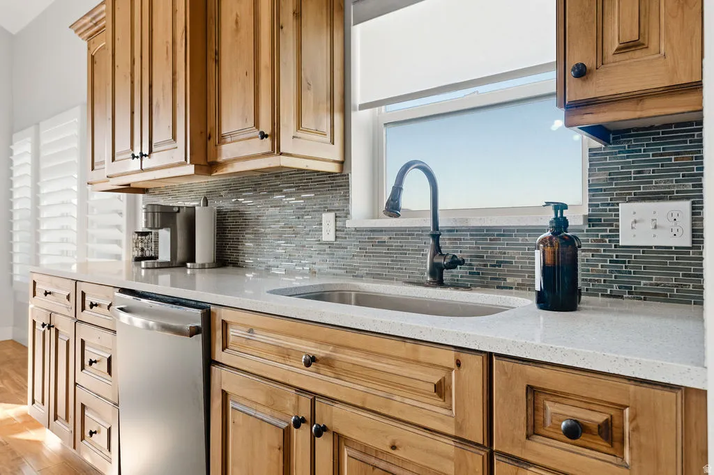 Kitchen featuring wood cabinetry, light-toned countertops, a stainless steel sink with a dark-finish faucet, and a mosaic tile backsplash