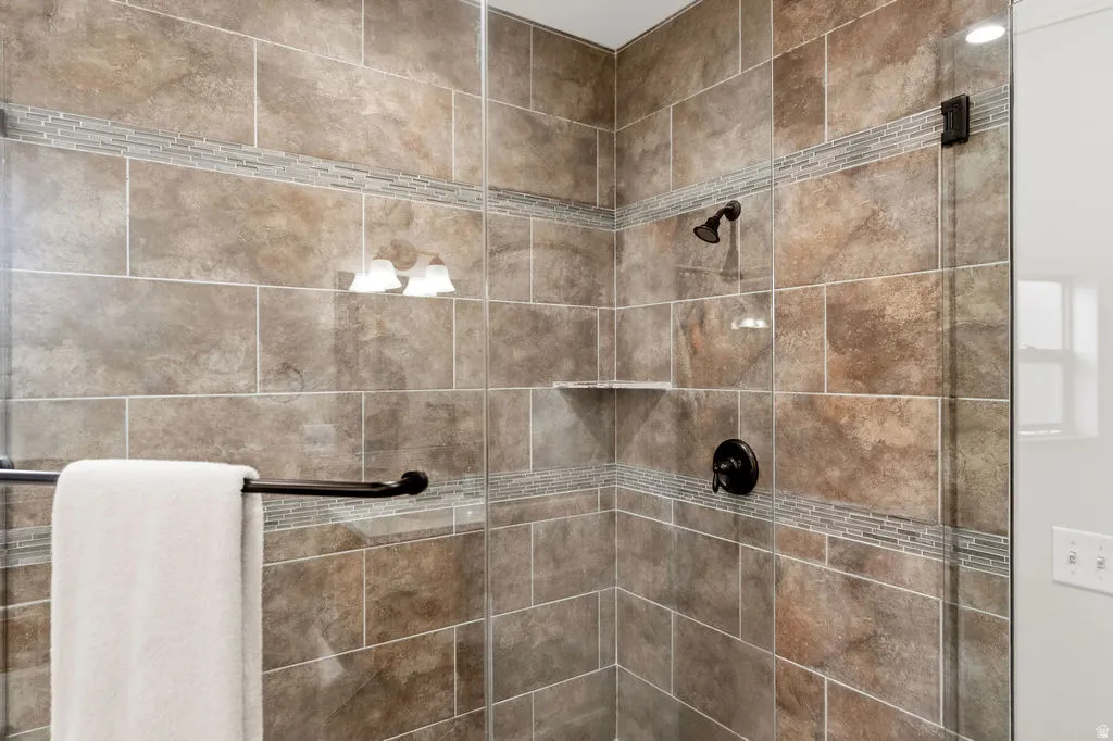 Tiled shower enclosure featuring a glass door, dark bronze fixtures, and an integrated shelf