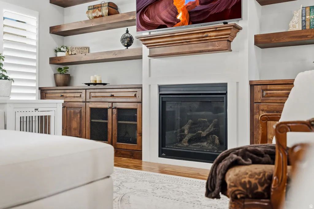 Built-in gas fireplace with a classic wood mantel, flanked by custom cabinetry with glass-front lower doors and open shelving