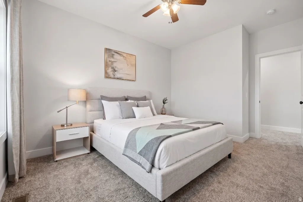 Carpeted bedroom featuring a ceiling fan with integrated lighting, a window with drapery, and a white interior door