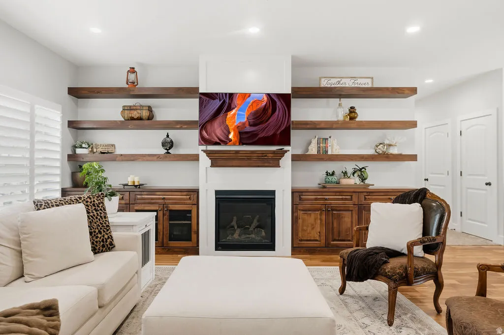 Living area featuring a fireplace with white mantle, built-in wooden cabinetry, floating wood-finish shelving, and wood-finish flooring
