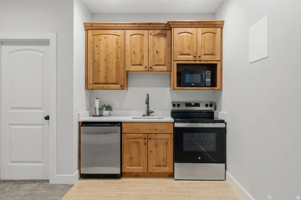 Compact kitchen area featuring wood cabinetry, stainless steel appliances, a built-in microwave, and a solid surface countertop with an undermount sink