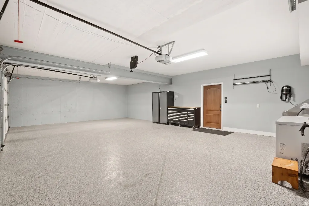 Spacious garage featuring a durable epoxy-coated concrete floor, neutral wall tones, overhead fluorescent lighting, and a solid wood entry door