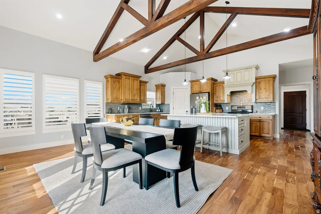 Vaulted ceiling with exposed wood beams, hardwood flooring, and a kitchen featuring light wood cabinetry