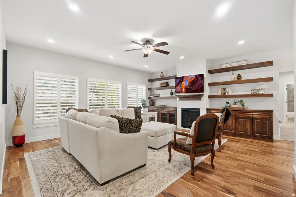 Spacious living area featuring wood-finish flooring, multiple windows with white plantation shutters, a ceiling fan, and recessed lighting