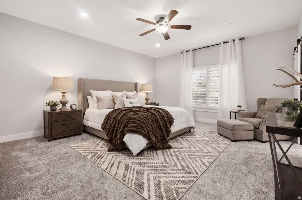 Bedroom featuring soft gray carpeting, a ceiling fan with integrated lighting, recessed lighting, and white window shutters with floor-length sheer curtains