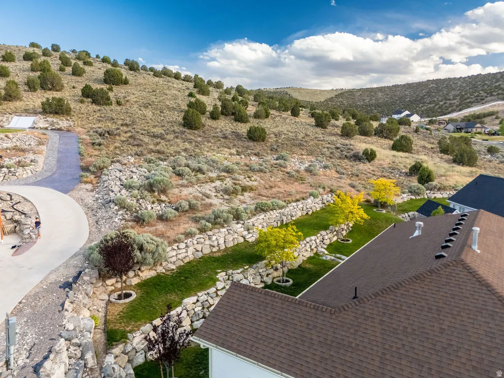 Landscaped hillside property featuring a paved walkway, tiered stone retaining walls, and planted trees