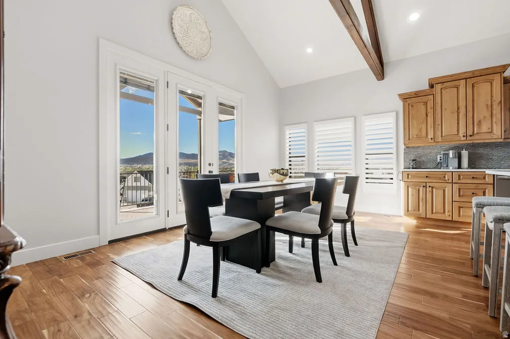 Open-concept dining area featuring vaulted ceilings with exposed wood beams, hardwood flooring, and three French doors leading to an outdoor space