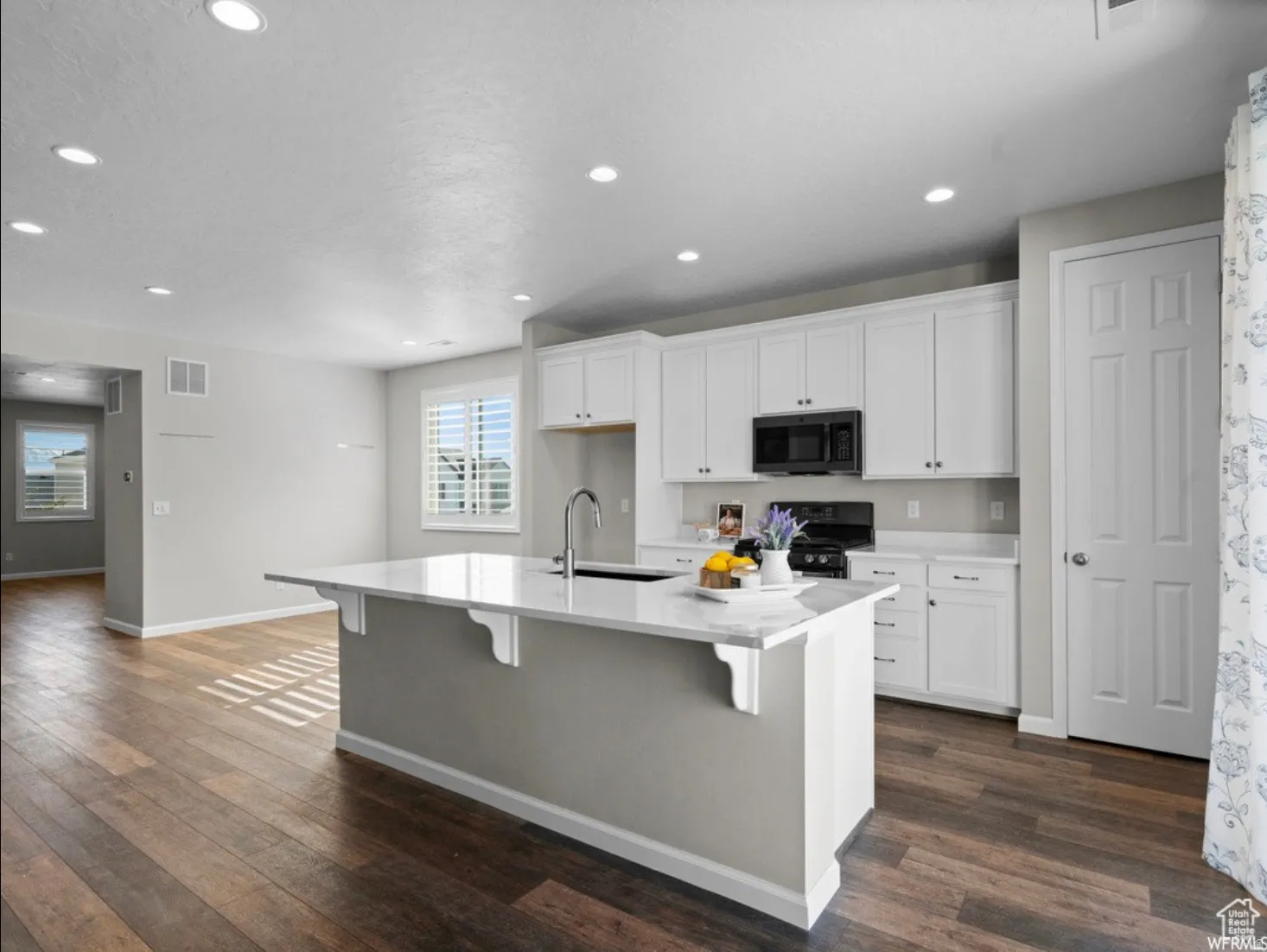 Open-concept kitchen featuring an island with a sink, white cabinetry, integrated black appliances, and wood-finish flooring
