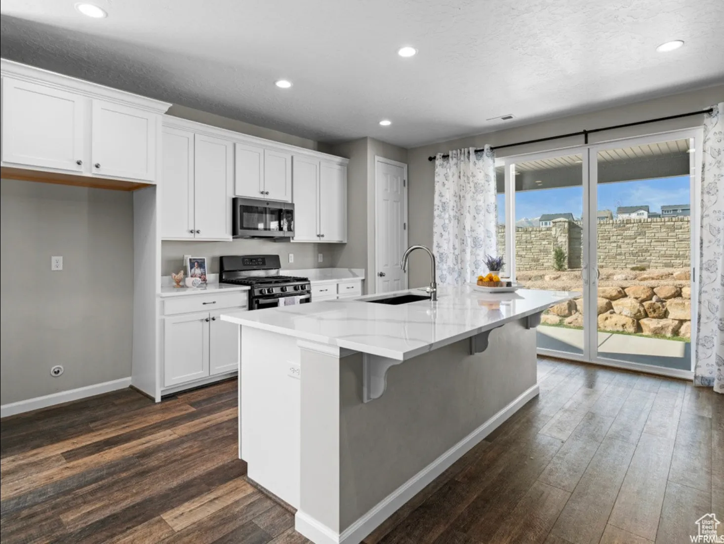 Open-concept kitchen featuring white shaker cabinetry, an island with an undermount sink, dark wood-finish flooring, recessed lighting, and sliding glass doors to the exterior