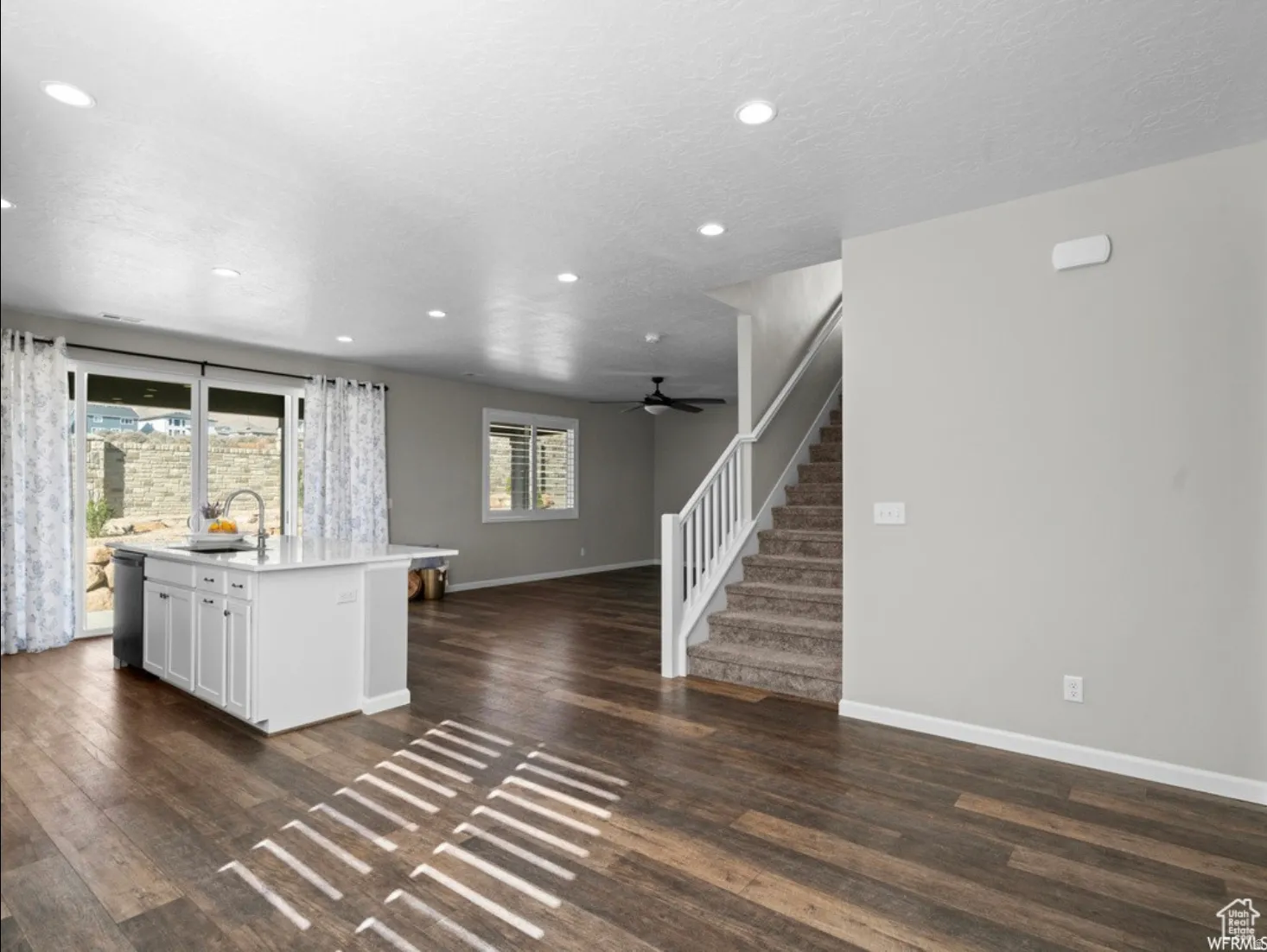 Contemporary kitchen island with a white countertop and built-in sink, recessed lighting, wood-finish flooring, sliding glass patio doors, and carpeted stairs with white railings