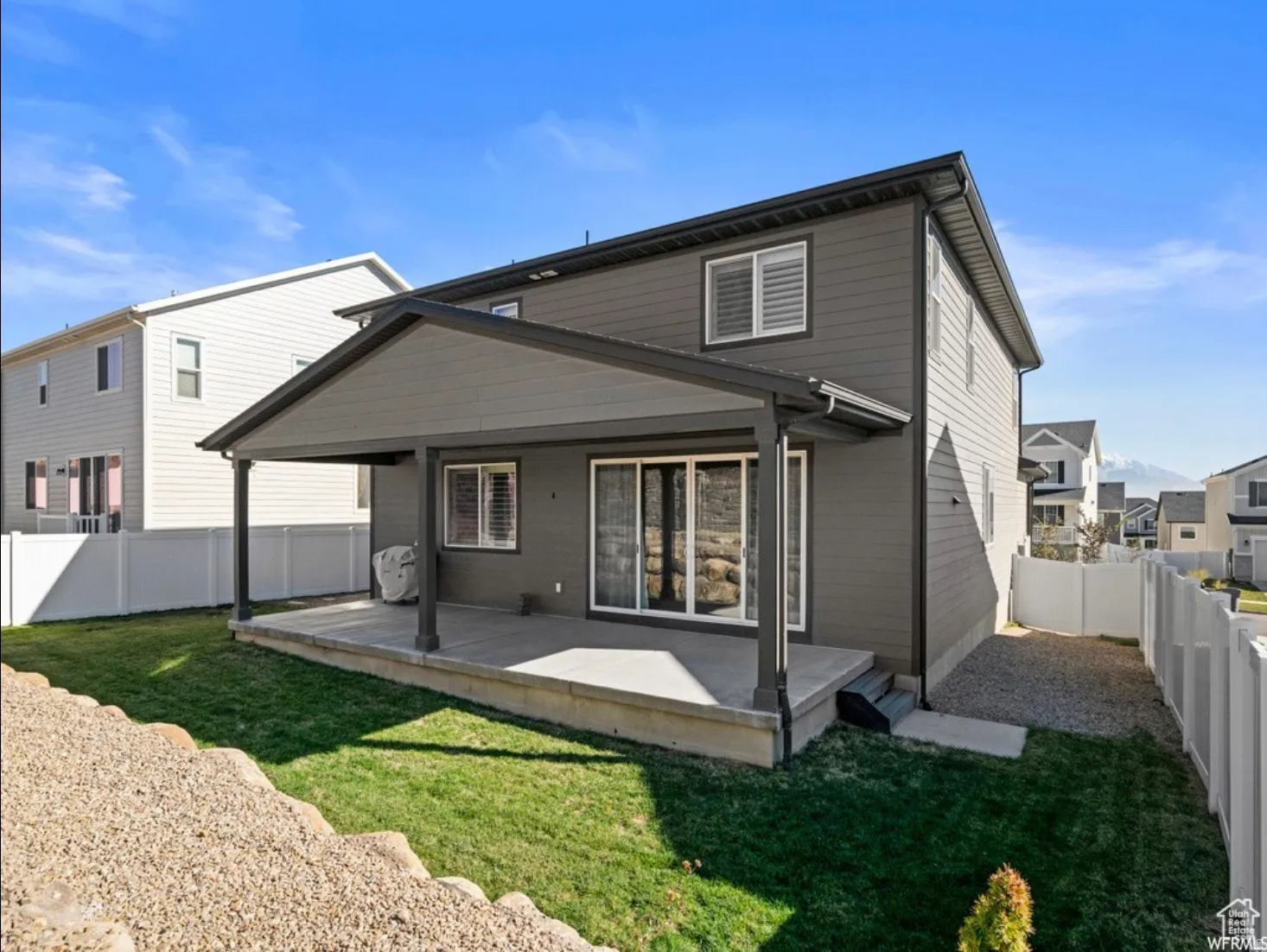 Rear exterior featuring a covered patio, sliding glass door, and a manicured lawn