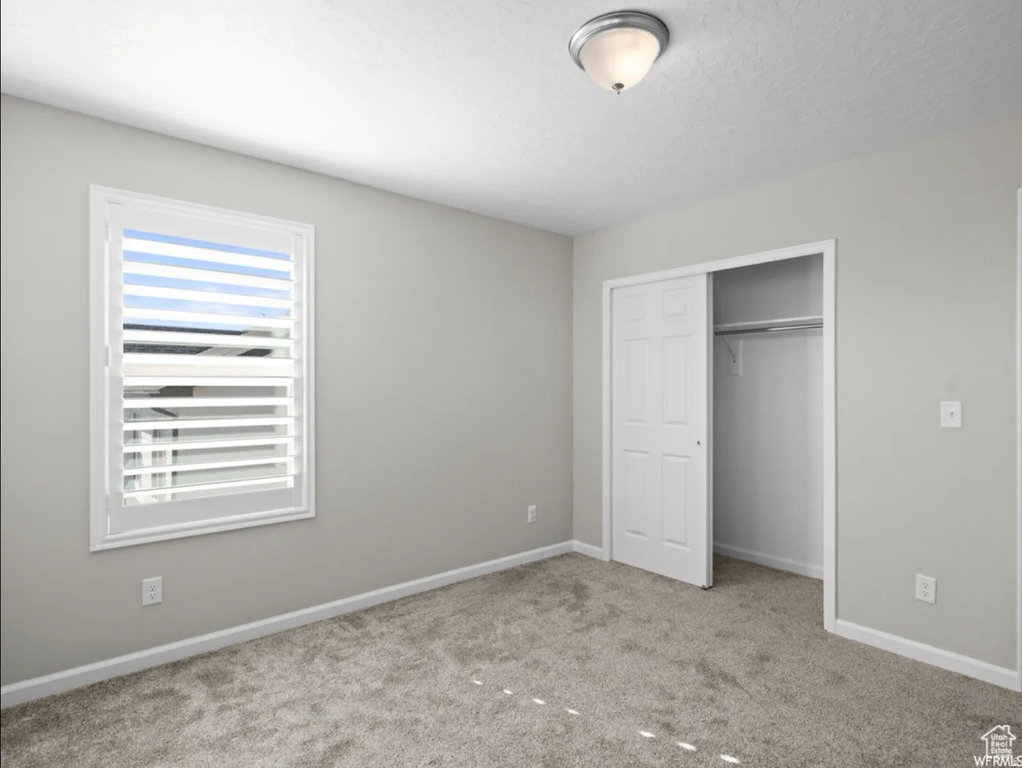 Carpeted room featuring a window with white louvered shutters, a flush-mount ceiling light, and a closet with bifold doors