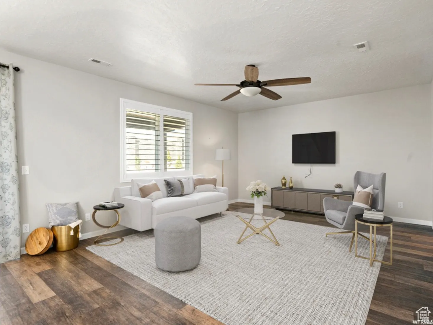 Spacious living area featuring wood-finish flooring, a ceiling fan with integrated lighting, and a large window with blinds