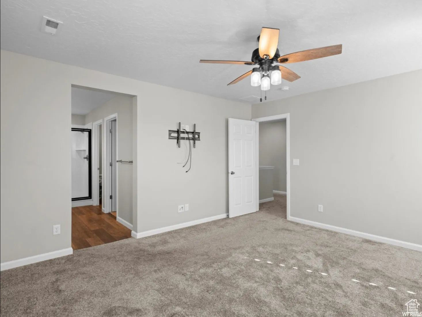 Neutral-toned room featuring a ceiling fan with light fixture, carpeted flooring, and a flat-panel television mount